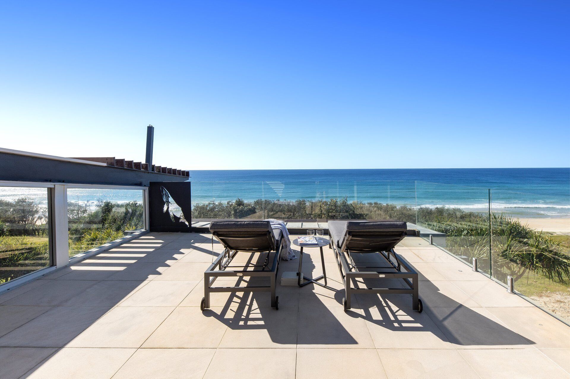 Une terrasse avec deux chaises longues et une table, offrant une vue sur une plage et l’océan.