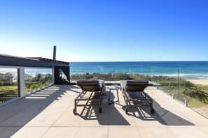 A terrace with two lounge chairs and a table, overlooking a beach and the ocean.