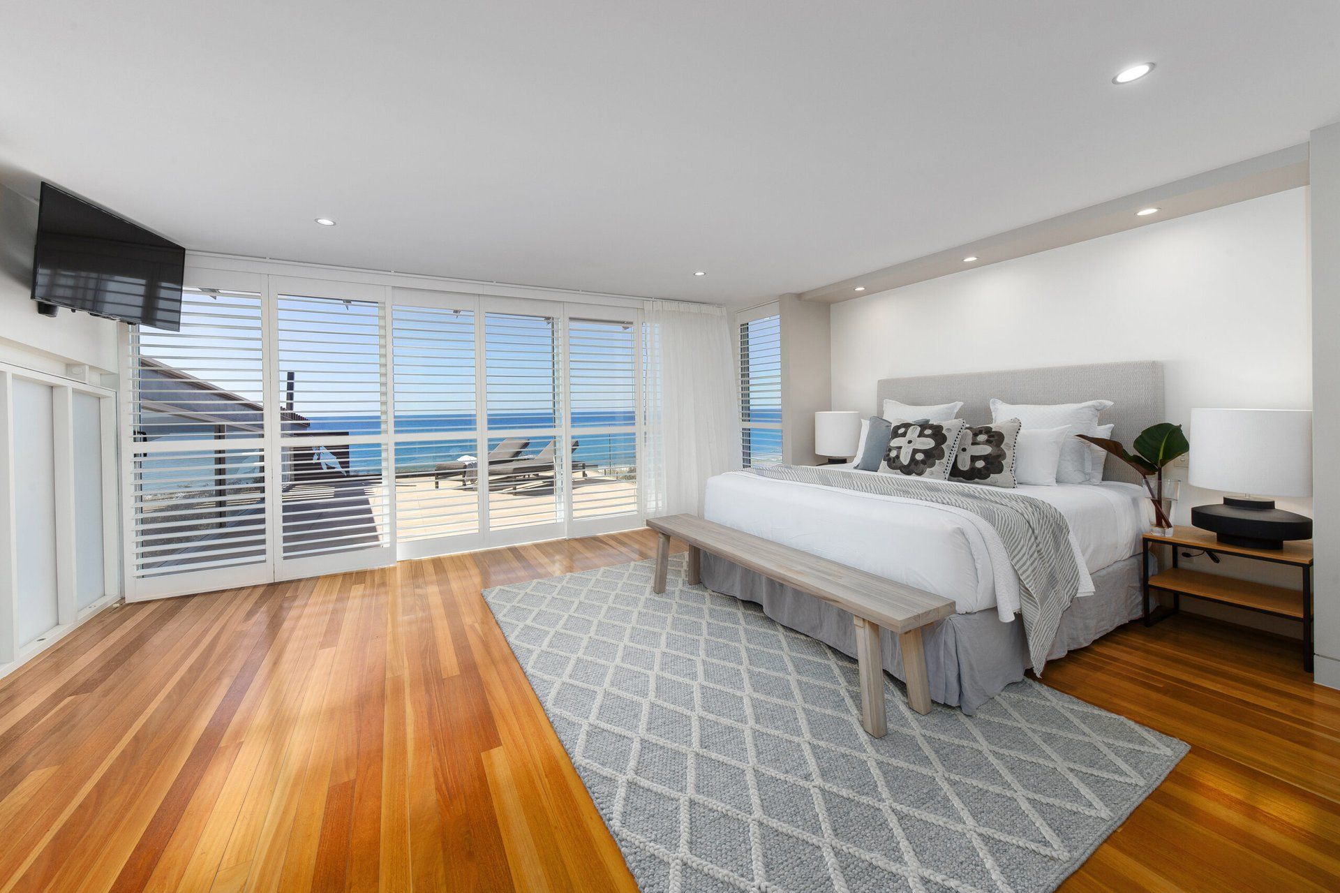 A bedroom with a large bed, a bench, a bedside table, and a TV.