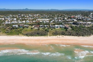 An aerial view of a coastal residential area with houses, a beach, and a mountain in the distance.
