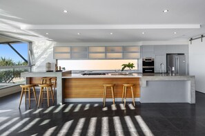 Cozinha moderna com ilha central, banquetas e vista para o exterior.