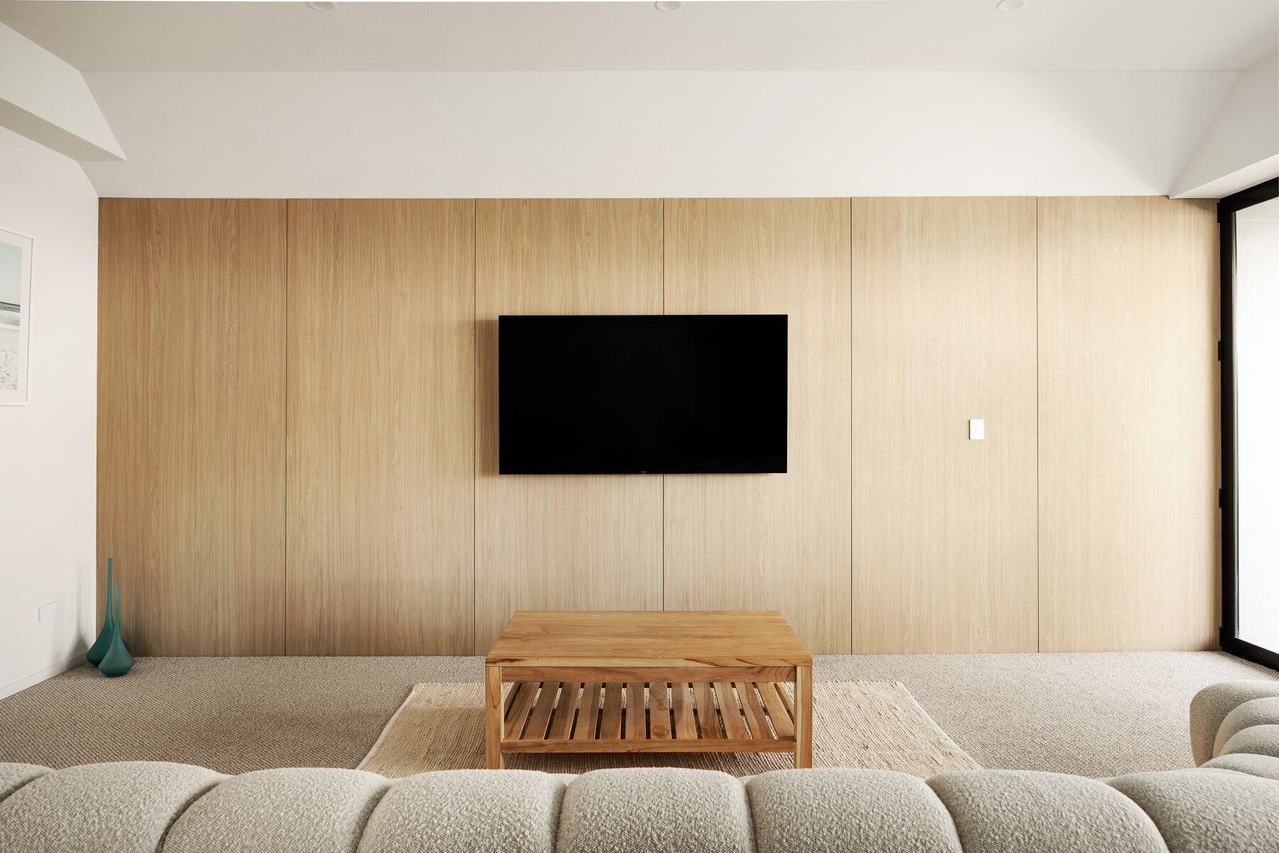 A modern living room with a flat-screen TV mounted on a wooden wall, a wooden coffee table, and a sofa.