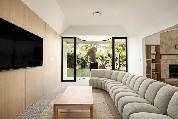 A modern living room with a curved sectional sofa, a flat-screen TV mounted on the wall, and a fireplace.