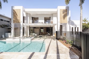 A modern two-story house with a swimming pool, outdoor seating, and a fenced garden area.