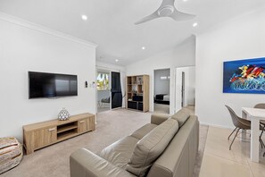 A modern living room with a flat-screen TV, a beige sofa, a wooden entertainment unit, and a ceiling fan.