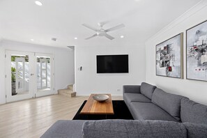 Een moderne woonkamer met een grijze bank, een houten salontafel, een flatscreen televisie en een plafondventilator.