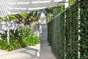 A pathway flanked by lush greenery and a white pergola structure.
