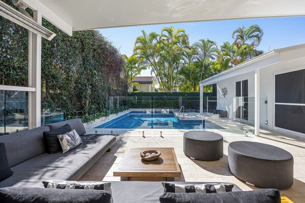 A modern outdoor living area with a pool, seating, and a view of palm trees.