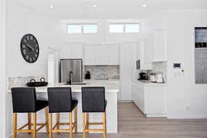 A modern kitchen with white cabinetry, a black clock, and a bar area with three chairs.