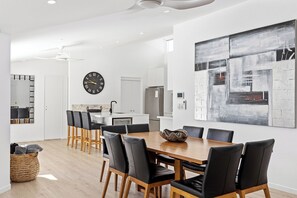 A modern dining area with a wooden table and black chairs, a kitchen with a stainless steel refrigerator, and a large abstract painting on the wall.