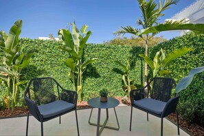 Een terras met twee stoelen en een tafel, omringd door weelderige begroeiing en een haag.