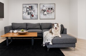 Een moderne woonkamer met een grijze bank, een houten salontafel met een theepot en een schaal, en twee abstracte schilderijen aan de muur.