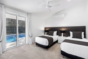 A hotel room with two beds, a ceiling fan, an air conditioning unit, and a view of a swimming pool through a glass door.