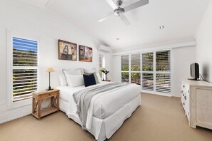 A bedroom with a bed, bedside tables, a ceiling fan, artwork, and a TV.