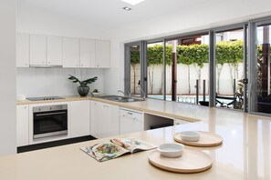 A modern kitchen with white cabinetry, a built-in oven, a sink, and a large window overlooking a garden.