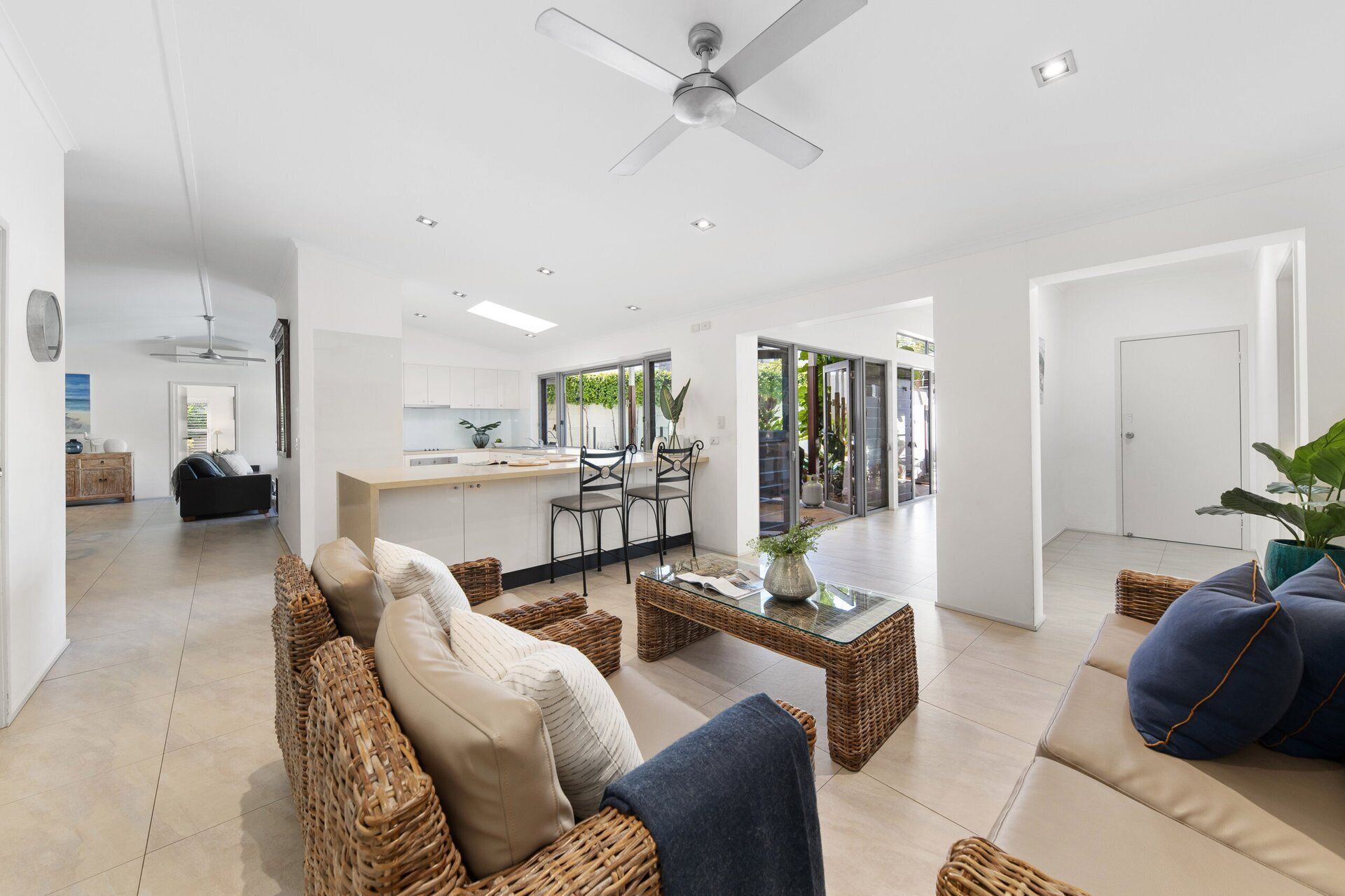 A spacious living area with a dining table, wicker furniture, and a ceiling fan.