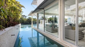 A modern outdoor pool area with glass walls, a seating area, and lush greenery. - Luxurious Riverfront Retreat (Noosa Heads)