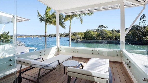 A sunlit deck with lounge chairs and a small table, overlooking a marina with boats and palm trees. - Luxurious Riverfront Retreat (Noosa Heads)