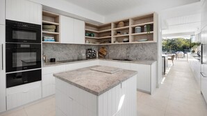 A modern kitchen with built-in appliances, open shelving, and a central island. - Luxurious Riverfront Retreat (Noosa Heads)