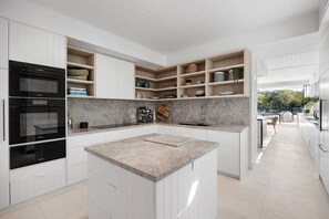 A modern kitchen with built-in appliances, open shelving, and a central island.