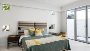 A bedroom with a large bed, a nightstand, a lamp, and a view of the outdoors through a sliding glass door. - Luxurious Riverfront Retreat (Noosa Heads)
