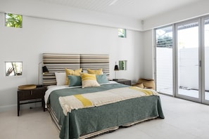 A bedroom with a large bed, a nightstand, a lamp, and a view of the outdoors through a sliding glass door.