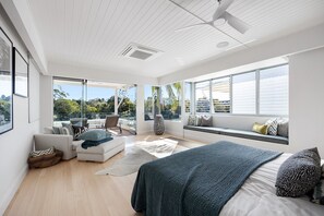 Een moderne slaapkamer met een groot bed, een zithoek met een bank en fauteuils, en uitzicht op het landschap door grote ramen.