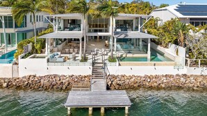 A modern house with a pool, outdoor seating, and a dock extending into the water. - Luxurious Riverfront Retreat (Noosa Heads)