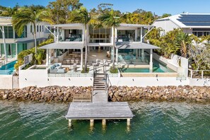 Een modern huis met een zwembad, terras en een steiger die in het water uitstelt.