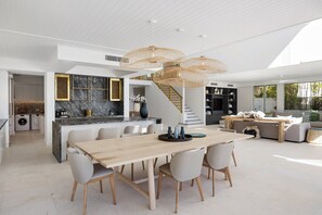 Een ruime woonkamer met een eettafel, stoelen en een trap naar een verdieping erboven.