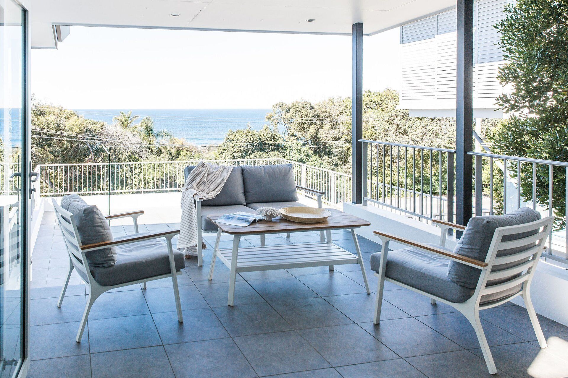 Un balcón con sofá, dos sillones, una mesa y vista al mar.