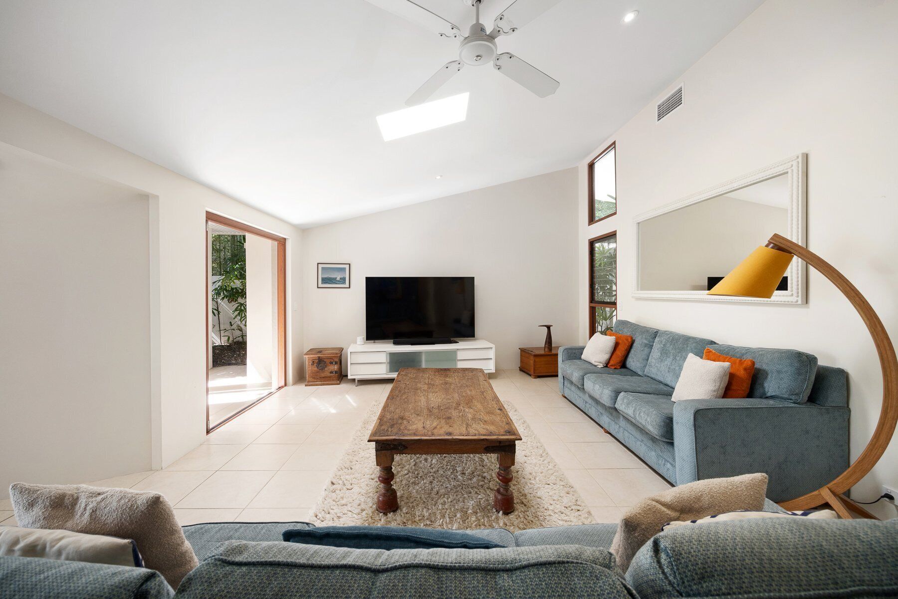 A modern living room with a flat-screen TV, a wooden coffee table, a blue sofa, and a large mirror.