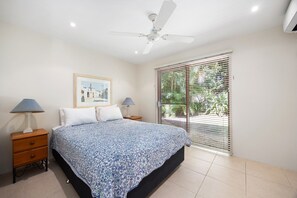 Ein Schlafzimmer mit einem Bett, zwei Nachttischen, einem Deckenventilator, einem Fenster mit Jalousien und einem gerahmten Bild an der Wand.