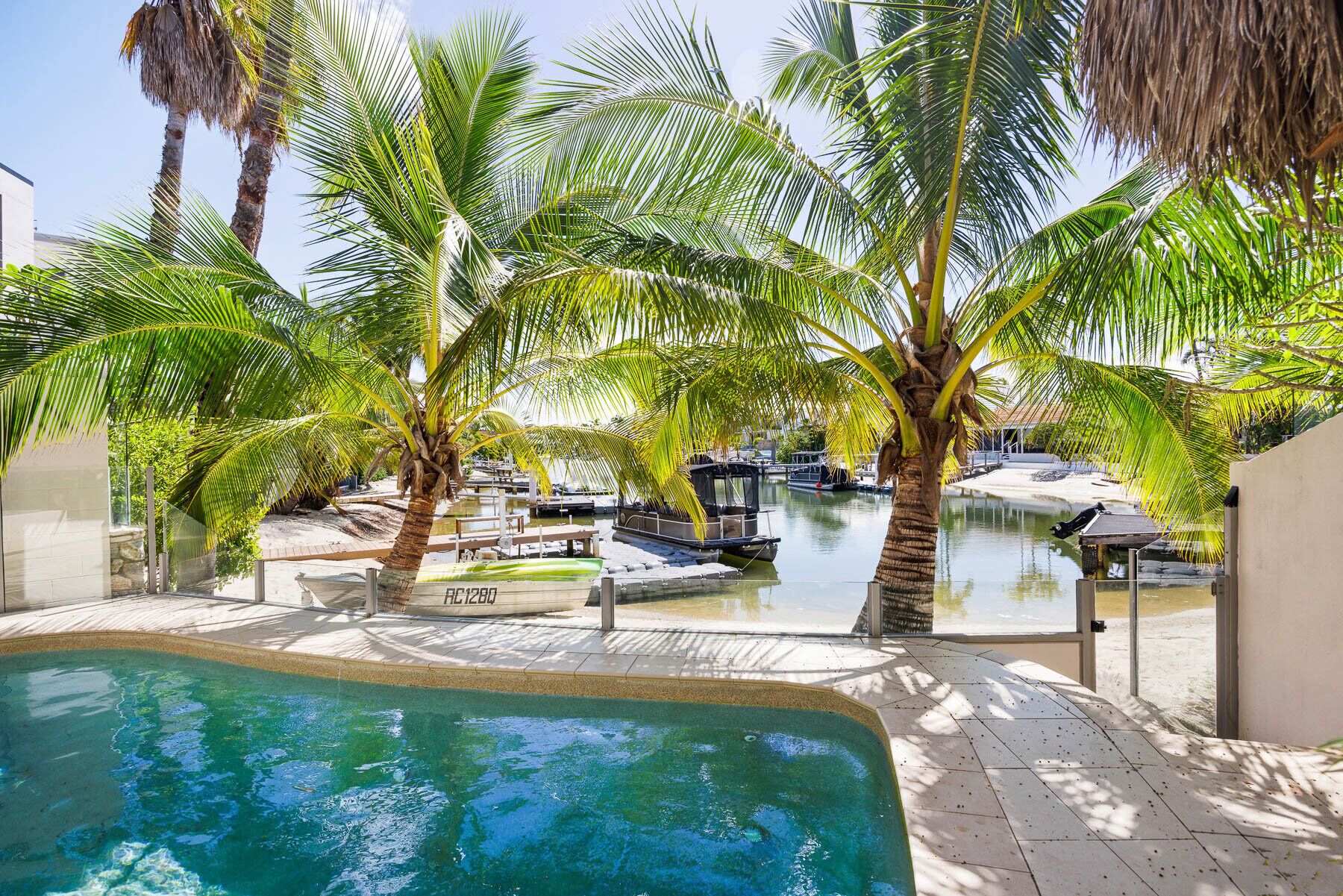 A pool area with palm trees, a boat dock, and a clear view of the water.