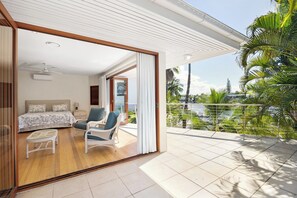 Relax on the balcony with a view of palm trees and a body of water, featuring a comfortable bed and seating area.