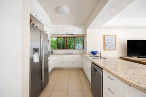 Eine moderne Küche mit weißen Schränken, einem Edelstahl-Kühlschrank, einem eingebauten Backofen und einem Fenster mit Blick ins Grüne.