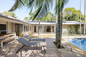 A modern outdoor pool area with lounge chairs, a wooden deck, and a view of a residential building with large windows and a covered patio. - Modern Oasis in Noosa Heads (Noosa Heads)
