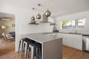 A modern kitchen with a large island, bar stools, a built-in oven, and a window with a view. - Modern Oasis in Noosa Heads (Noosa Heads)