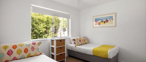 Un dormitorio con dos camas, un ventilador de techo, una ventana con vistas a árboles y un cuadro en la pared.