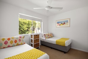 A bedroom with two beds, a ceiling fan, a window with a view of trees, and a framed picture on the wall. - Modern Oasis in Noosa Heads (Noosa Heads)
