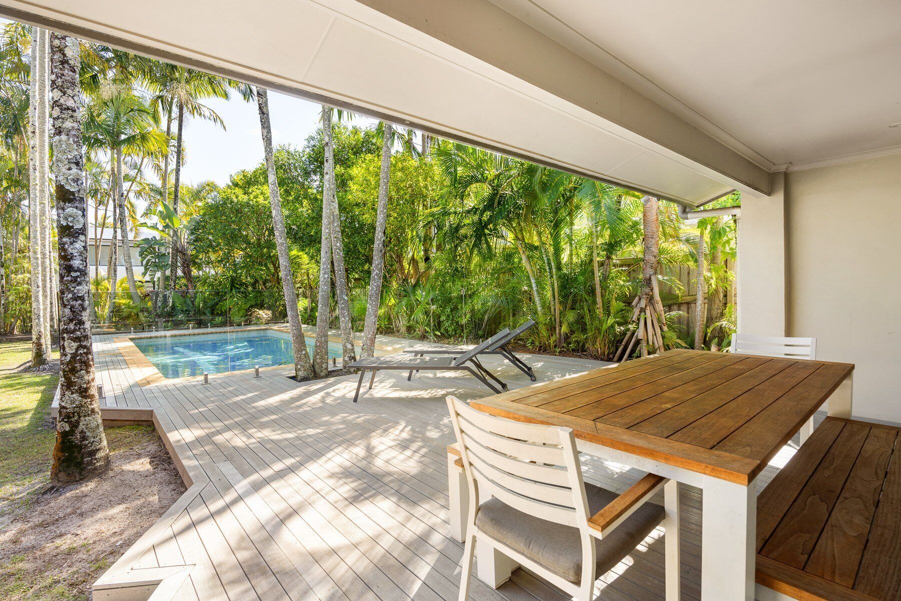 Um deck de madeira com piscina e espreguiçadeiras, rodeado por vegetação tropical.