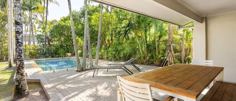 Eine Holzterrasse mit Pool und Liegestühlen, umgeben von tropischer Vegetation.
