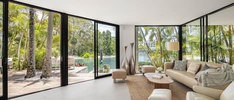 A modern living room with large glass doors leading to a pool and lush greenery.