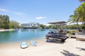 A beachside view with a clear sky, a boat docked on the water, lounge chairs, and a building in the background. - Luxury Retreat with Private Beach & Jetty (Noosa Heads)