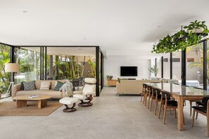 A modern living room with a sofa, coffee table, and dining area with chairs. - Luxury Retreat with Private Beach & Jetty (Noosa Heads)