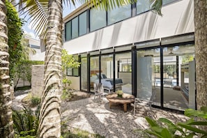 A modern house with a large glass window, a patio with a round table, and a pool area visible through the windows. - Luxury Retreat with Private Beach & Jetty (Noosa Heads)