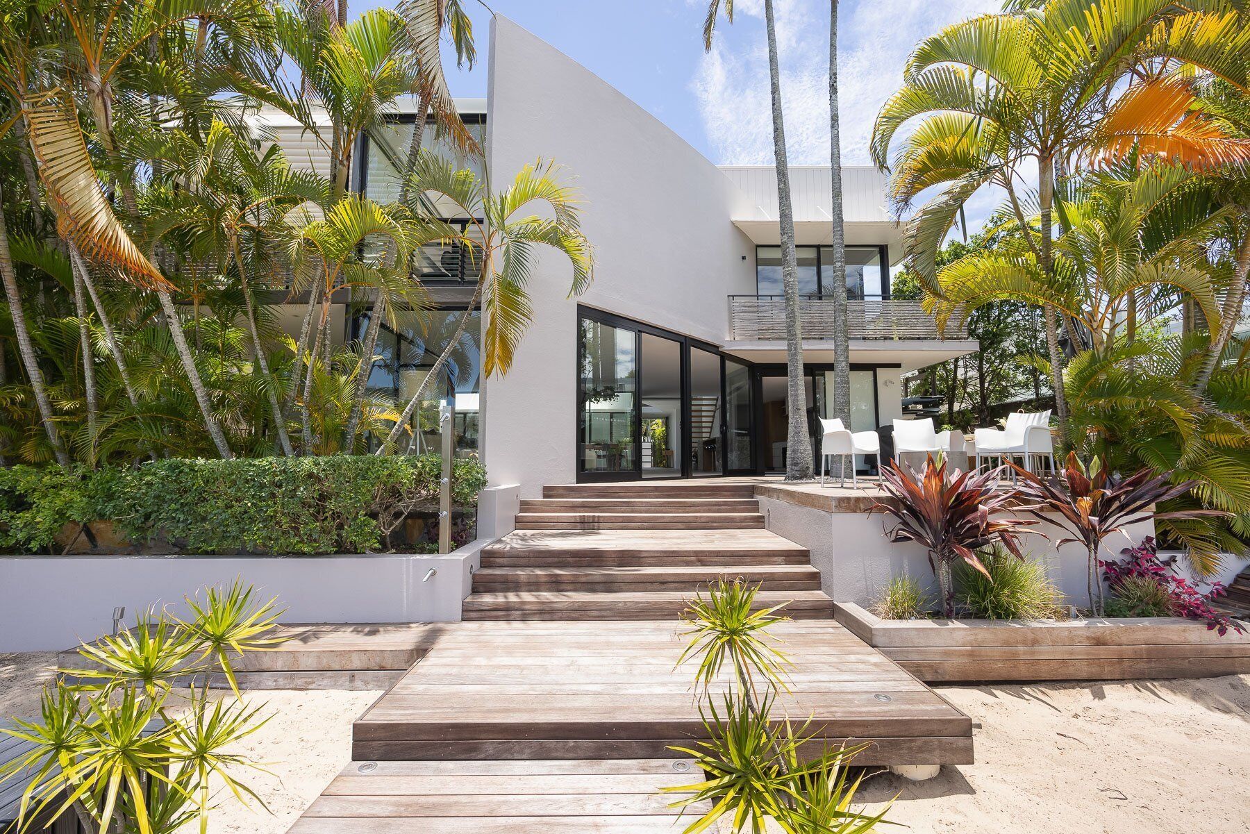 Um edifício moderno com fachada curva, deck de madeira que leva à entrada e plantas tropicais ao redor da área.