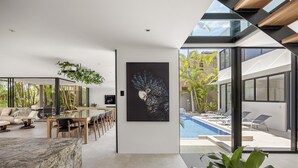 A modern interior with a dining area, a large painting, and a view of a swimming pool and outdoor area. - Luxury Retreat with Private Beach & Jetty (Noosa Heads)