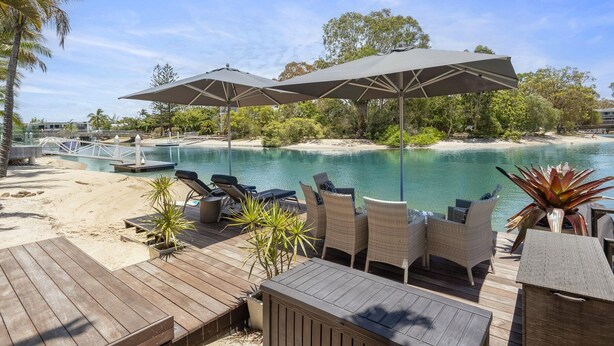 A poolside area with lounge chairs and umbrellas, a wooden deck, and a view of a beach and water. - Luxury Retreat with Private Beach & Jetty (Noosa Heads)