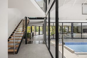 A modern interior with a glass-enclosed staircase leading to a pool area. - Luxury Retreat with Private Beach & Jetty (Noosa Heads)